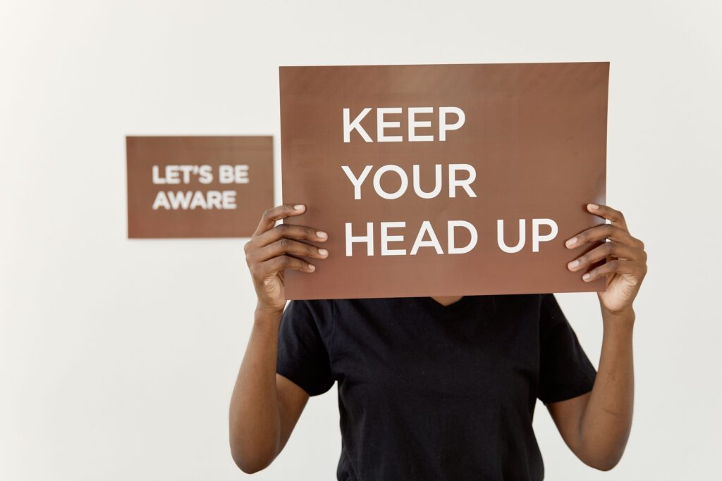 A motivational sign reading 'KEEP YOUR HEAD UP' held by a person indoors.